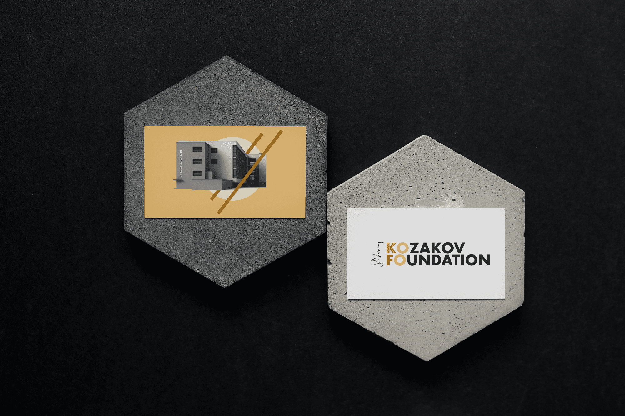 Two business cards designed by House Of Five Studio, showing a Bauhaus-style building on a pastel-yellow background and white-background card with a colourful and black and white Kozakov Foundation logo, both set on a stone hexagone and a black background.