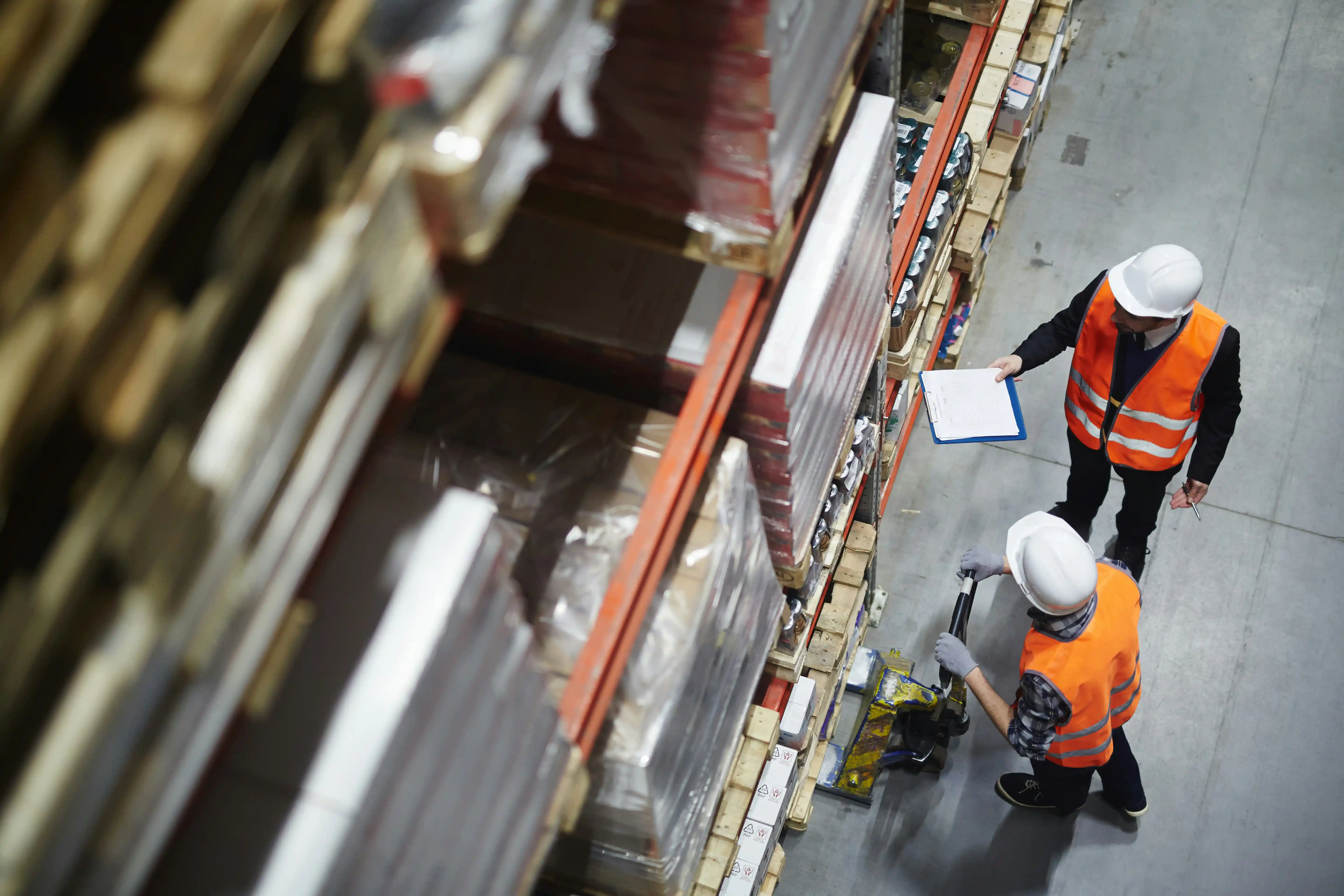 two men in bright orange high-vis jackets point at warehouse shelving