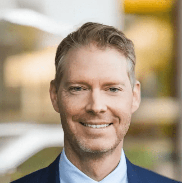 Timo Neustock, Geschäftsführer der ABENA GmbH, Portrait eines Mannes im blauen Anzug und Krawatte vor modernem Bürohintergrund.