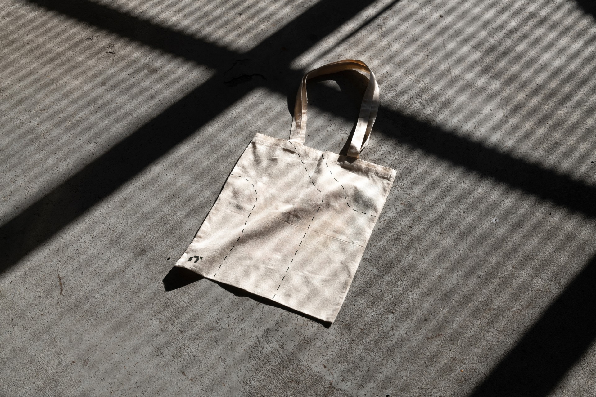 Ecobag clara com alça de couro posicionada sob sombra projetada.