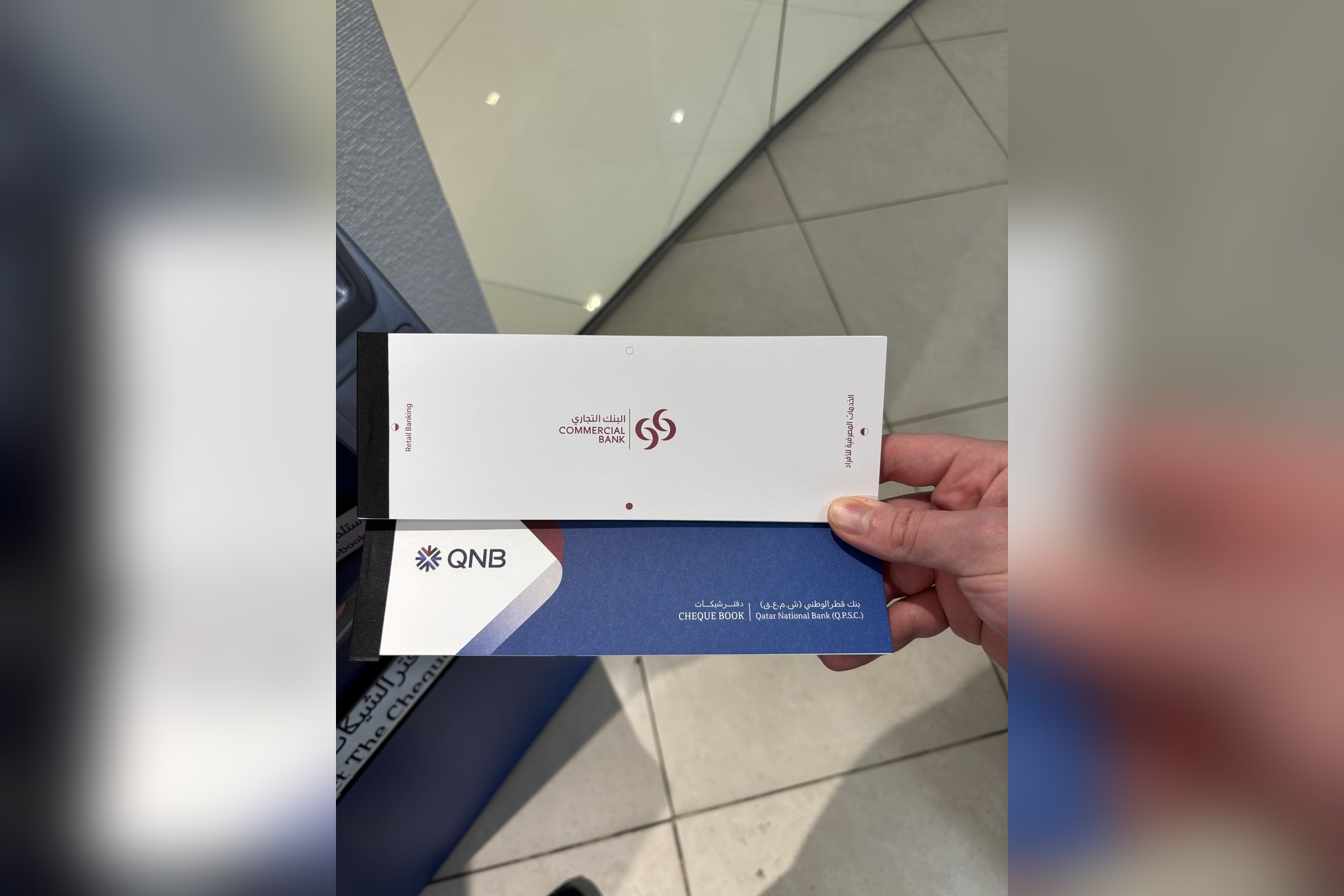 Deux chéquiers, Commercial Bank et QNB, tenus à la main au Qatar