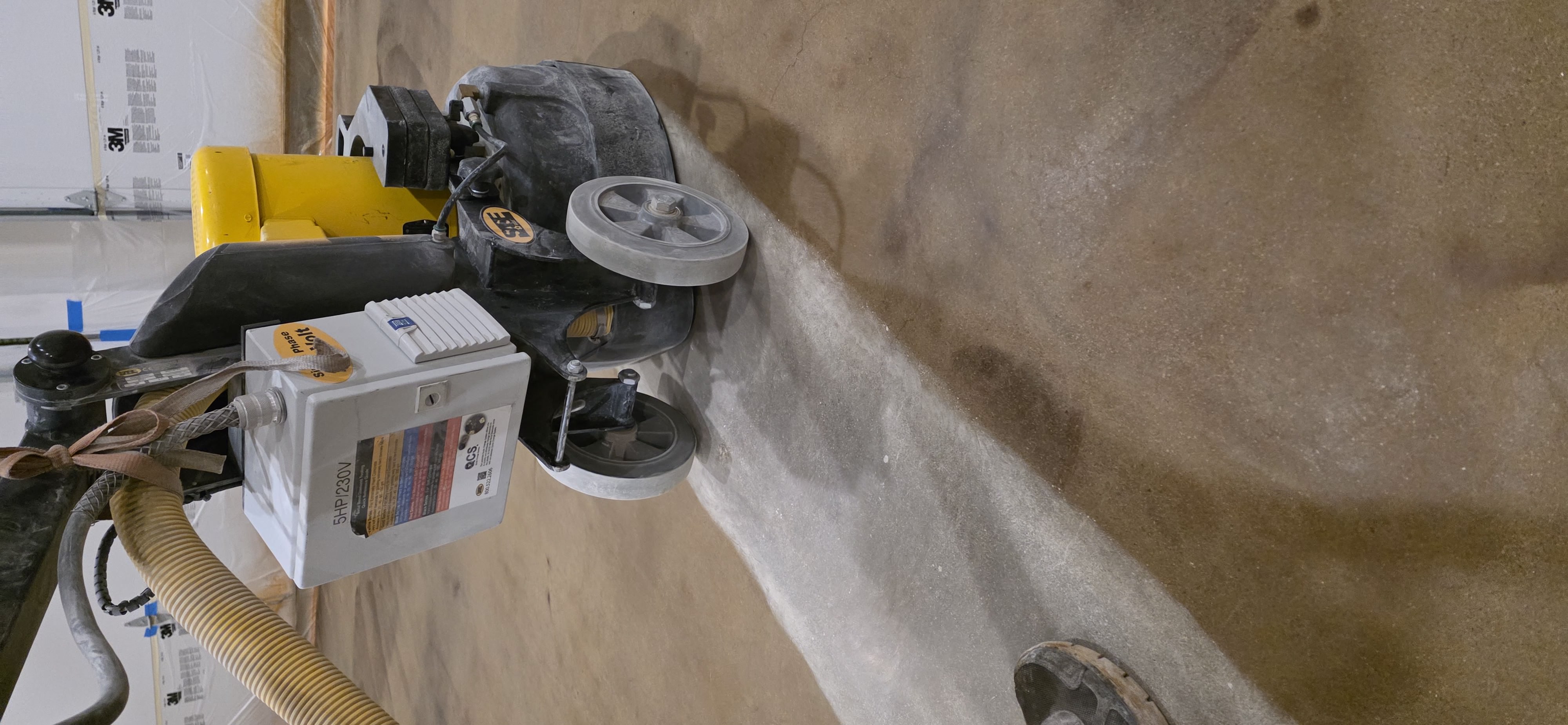 A close view of professional floor-preparation equipment grinding a strip of concrete.