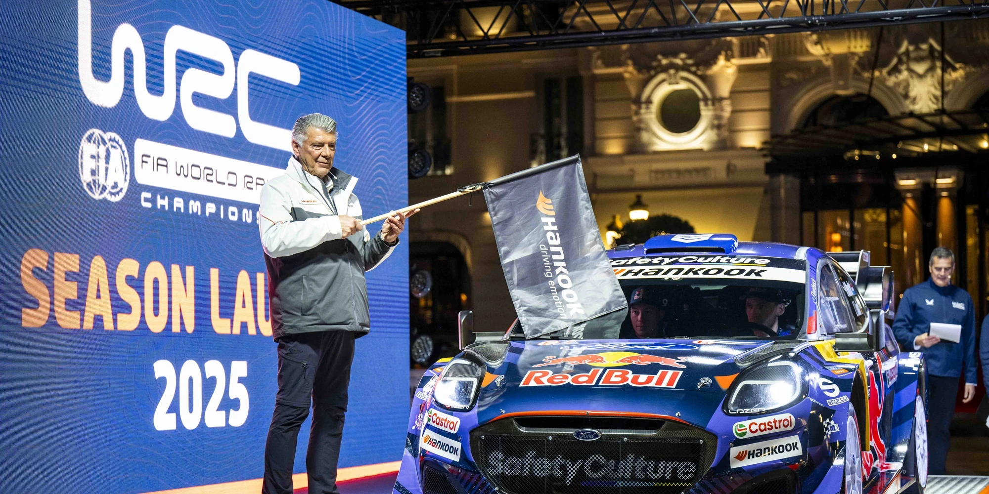 Man holding flag in front of rally car on a stage