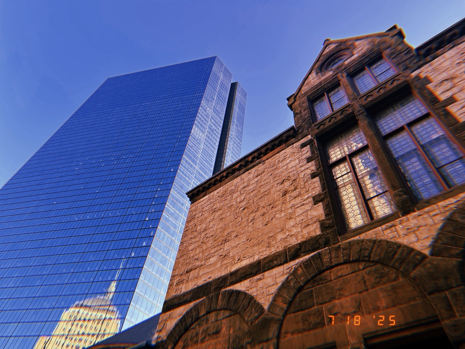 A glass tower beside a stone building Photograph by Pranjali Shah.