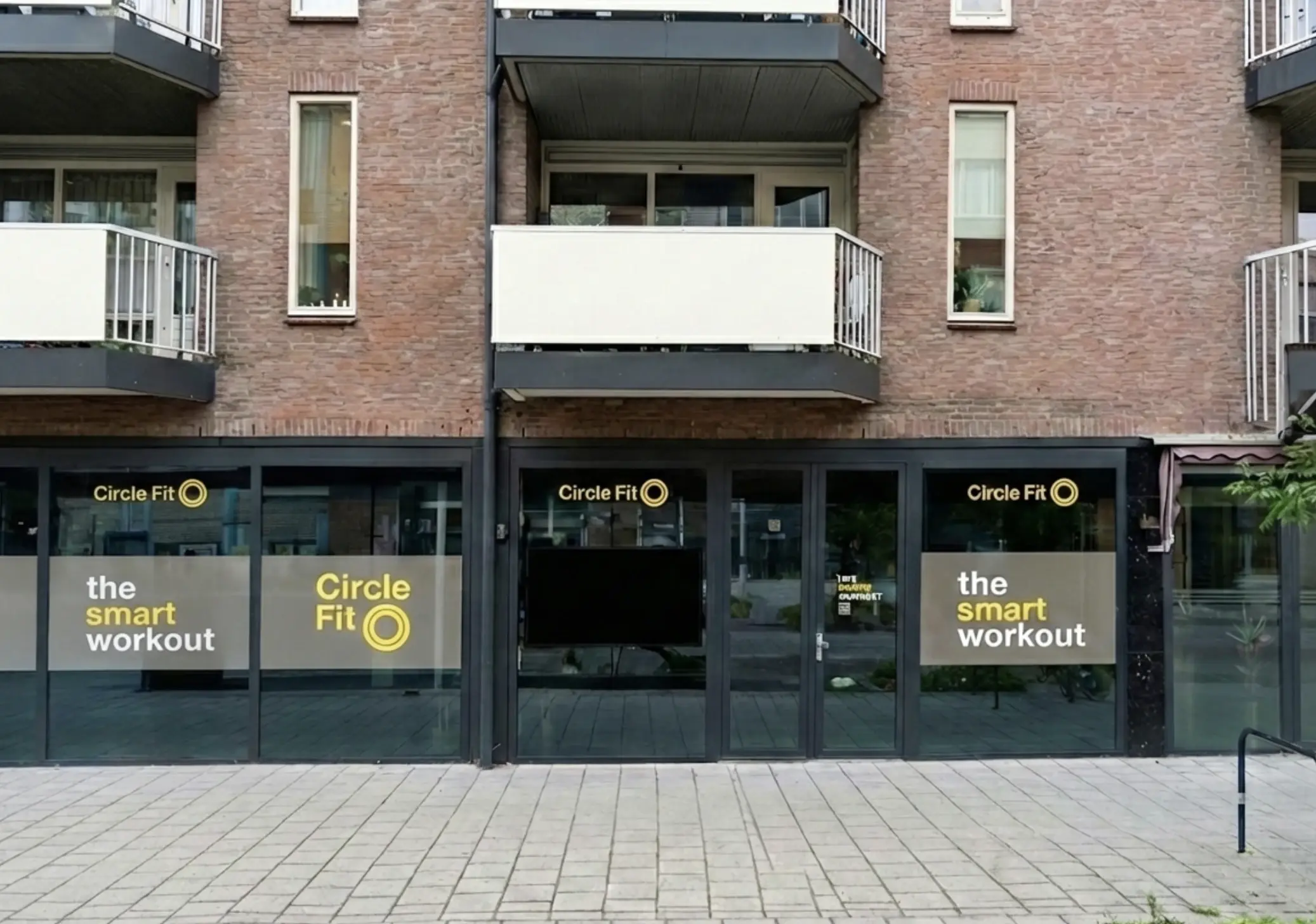 Een Circle Fit-hub met grote ramen die heldergele borden en promoties tonen, gezien vanaf het trottoir.