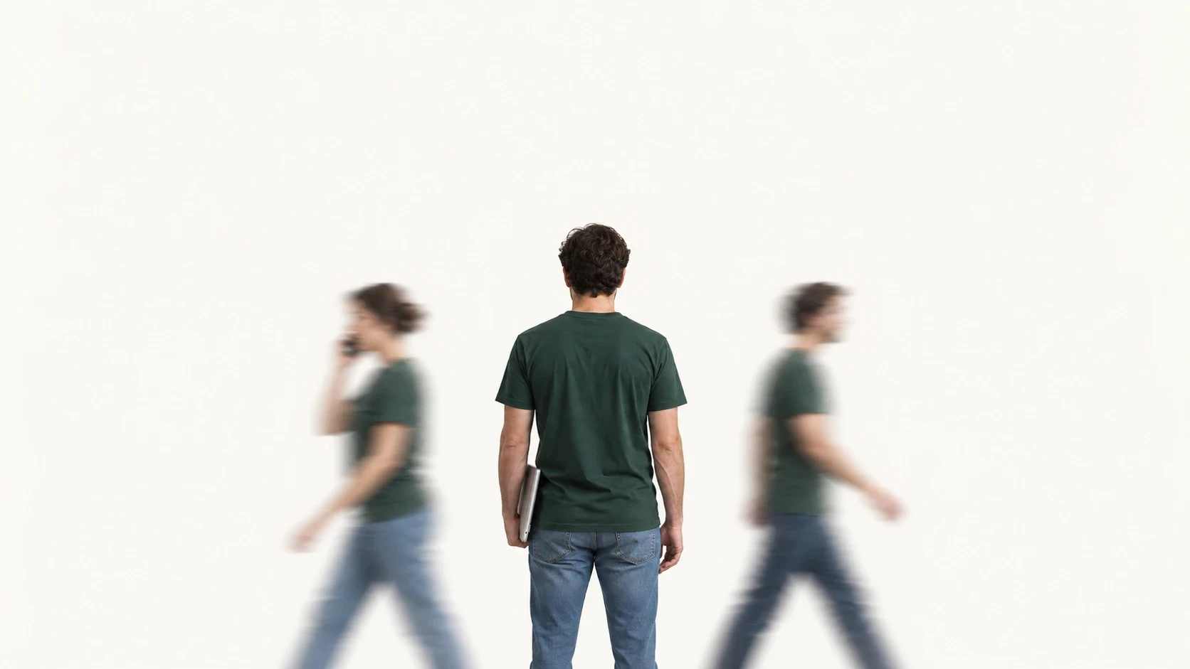 A person seen from behind with a laptop under one arm, two people walk past out of focus.