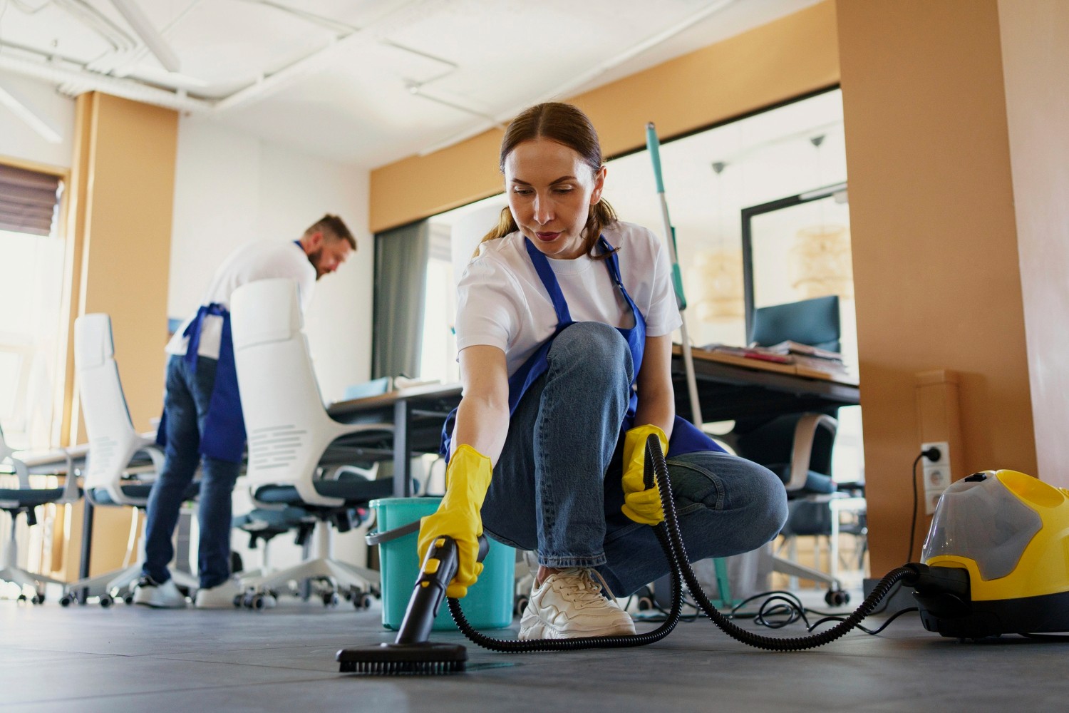 Person cleaning the floor with a green microfiber mop, wearing beige pants and sneakers, showcasing a modern and efficient cleaning method in an office setting.