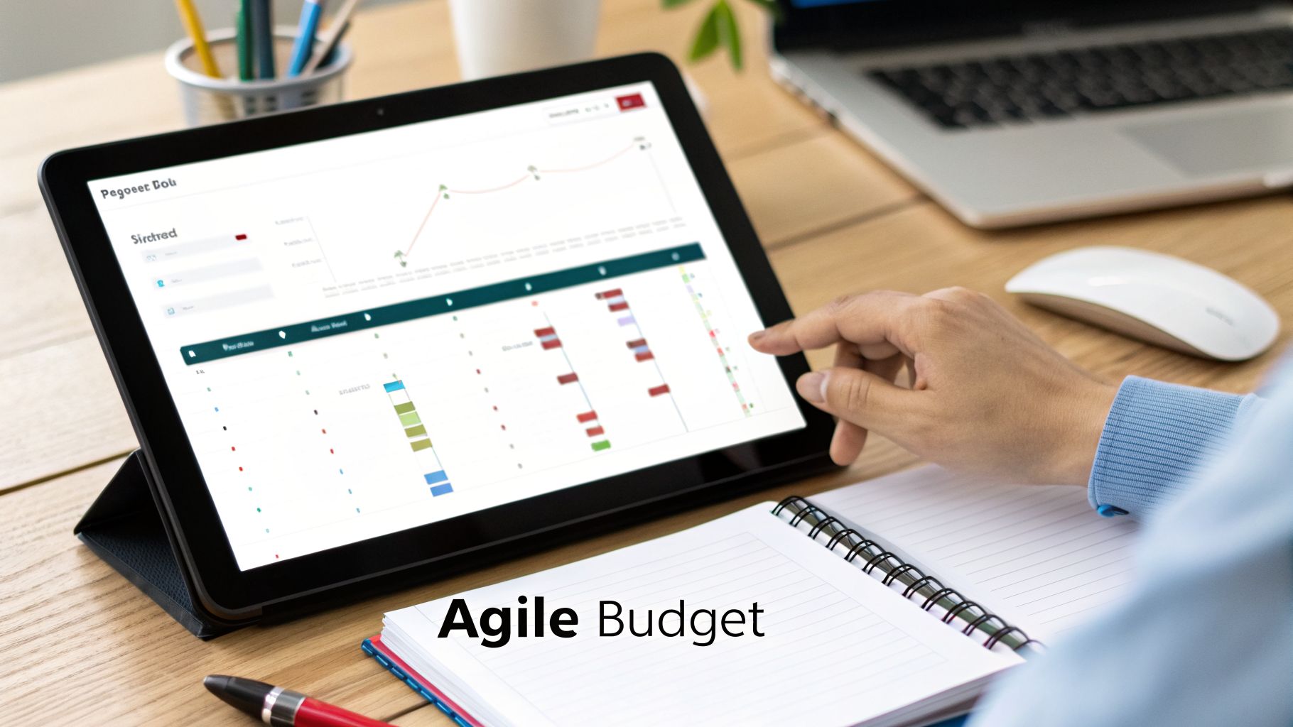 A person's hand interacting with a tablet displaying charts and business data, with an 'Agile Budget' notebook.