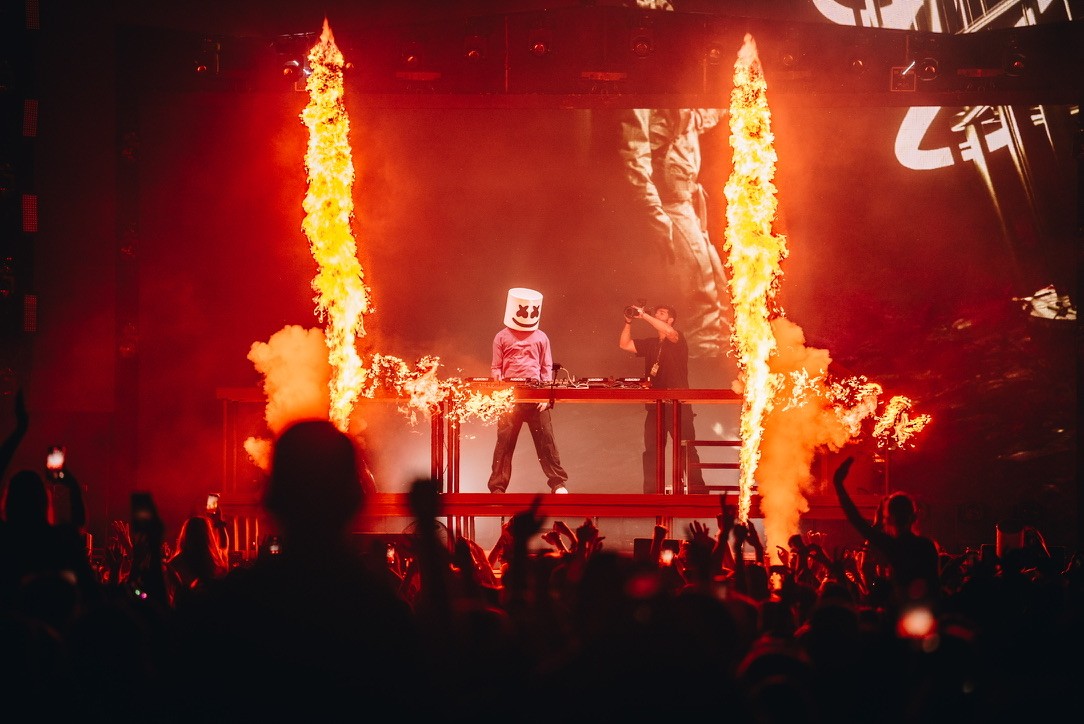 Marshmello tours in Europe with flames around him as a videographer records from behind