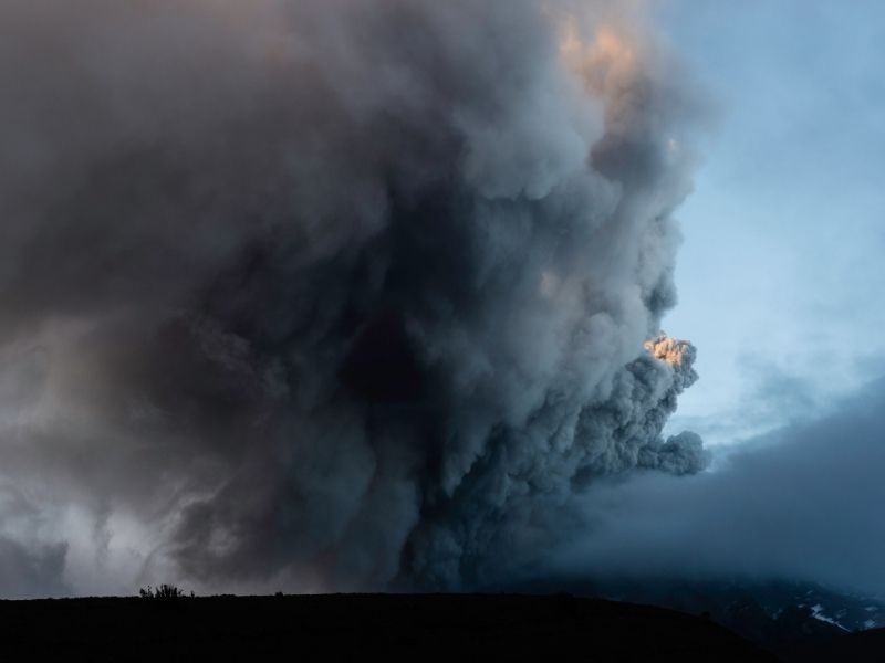 Dense column of ash and steam rising from Cotopaxi volcano in Ecuador during an explosive eruption, with dark clouds billowing into the sky.