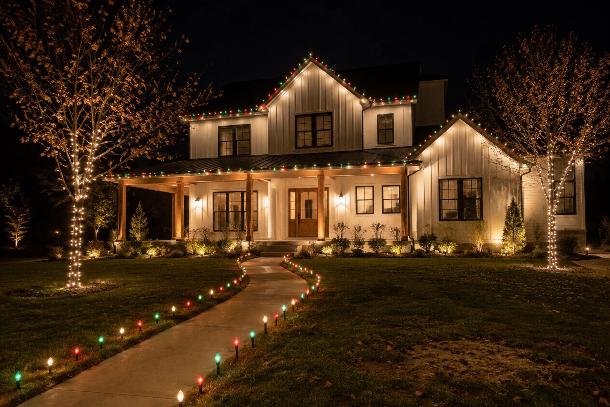 Home with a color-lit walkway and wrapped trees