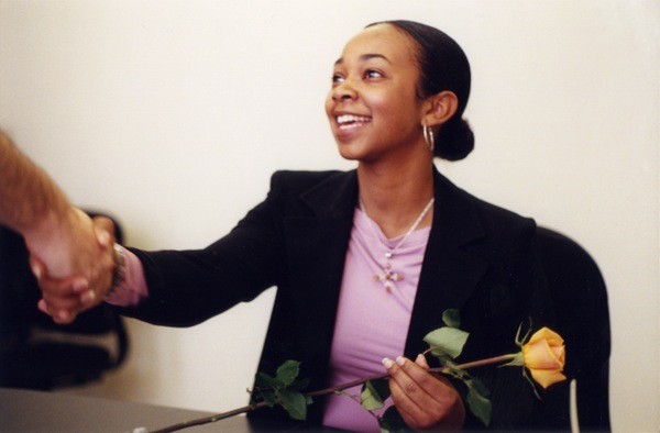 A photo of a woman shaking someone's hand while holding a rose in the other hand.