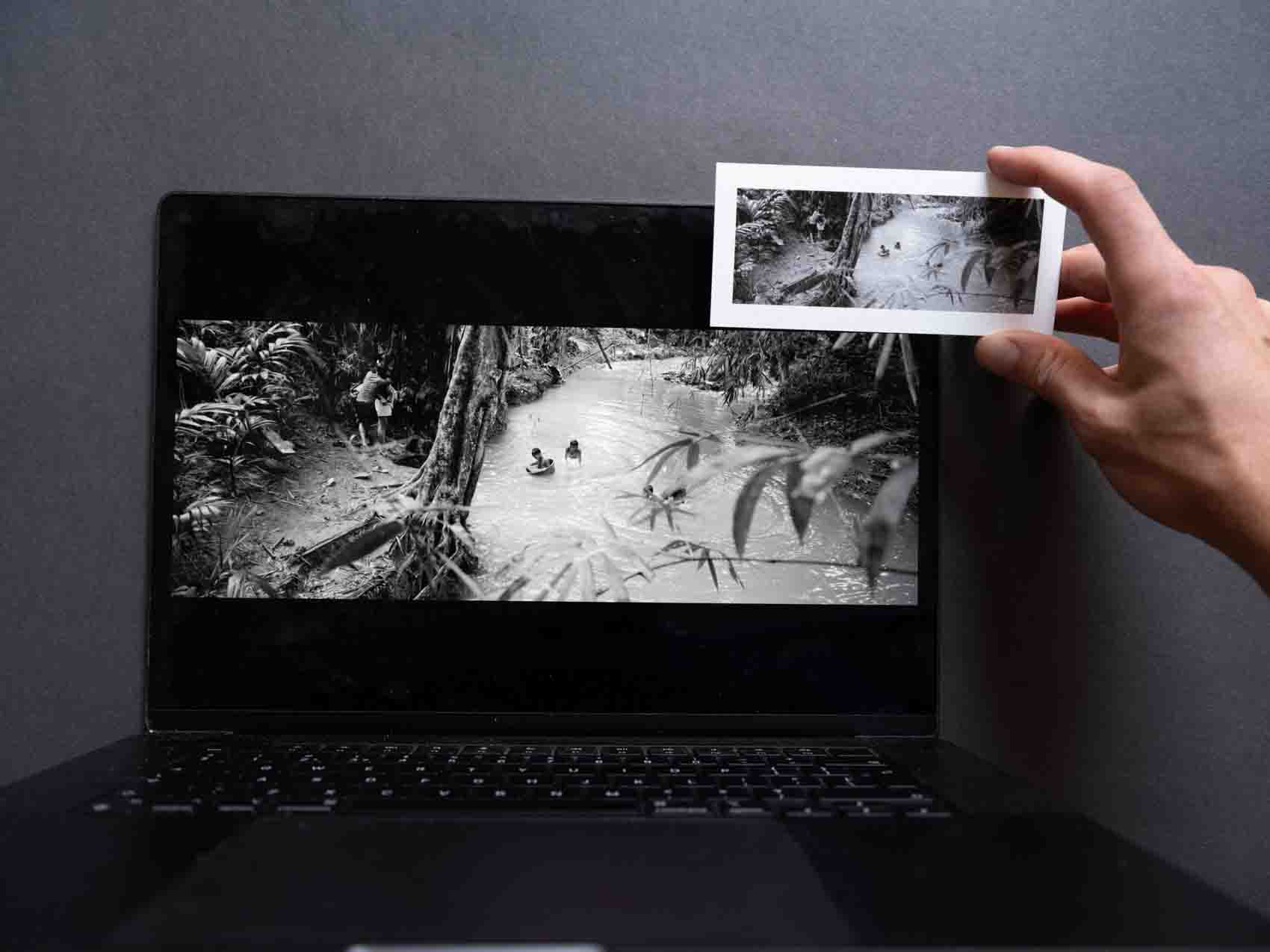 A tiny panoramic photo print of a kid playing in a river in the Philippines held in front of a laptop with the digital file for comparison