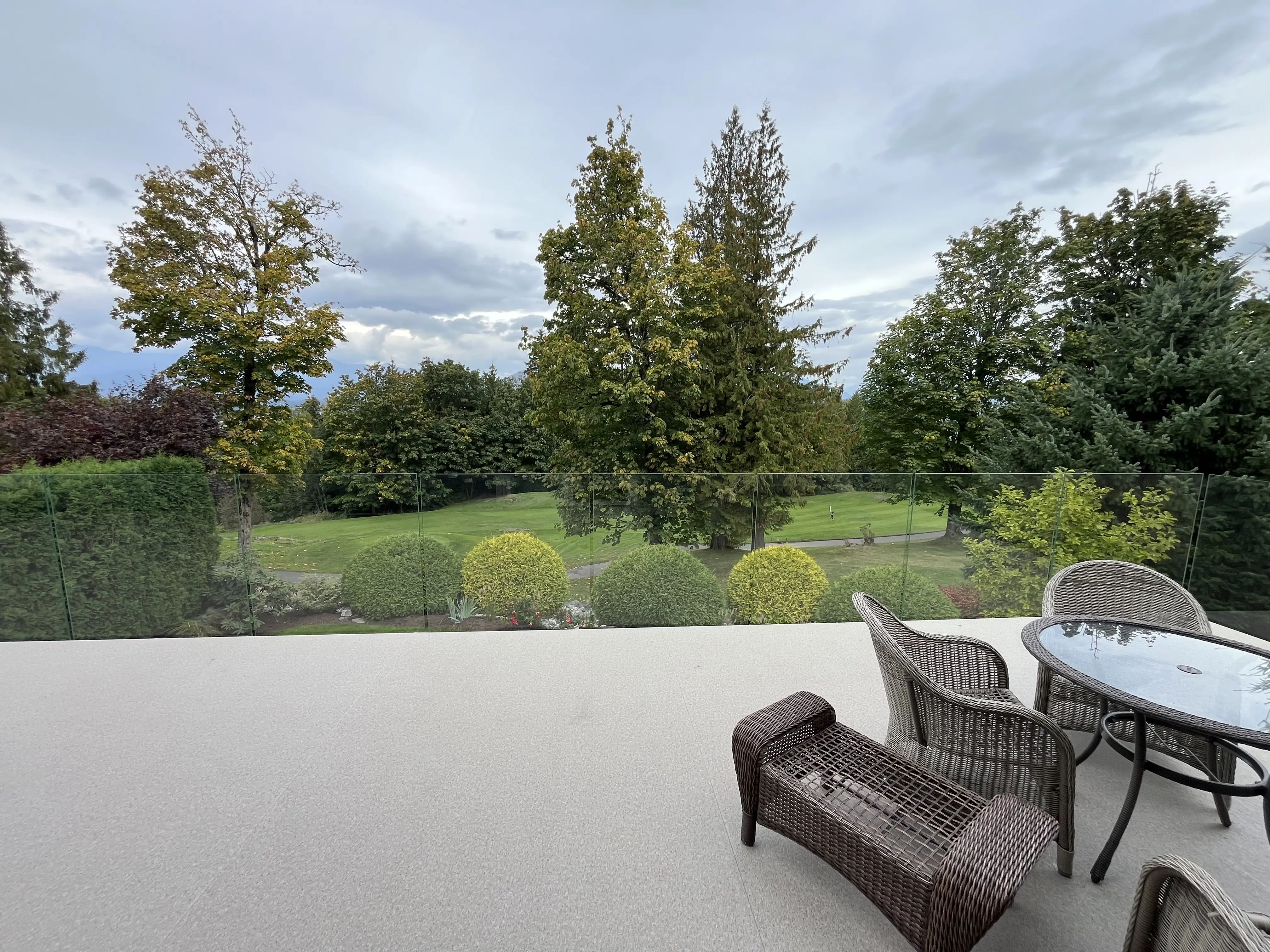 Frameless glass deck railing replacing a picket guard, keeping the fairway and garden sightline open