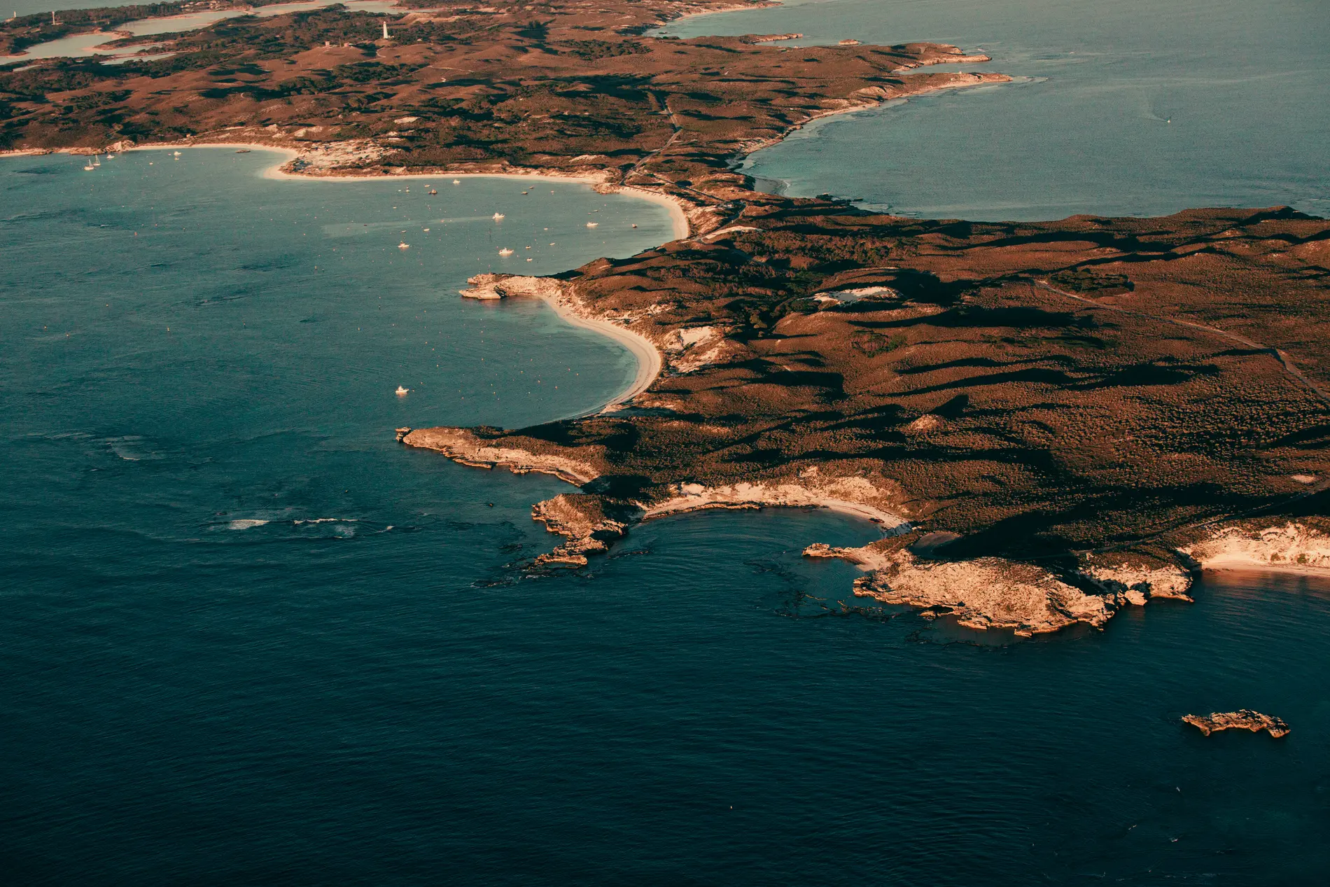 Aerial of an island coastline with sandy bays, moored boats and reef