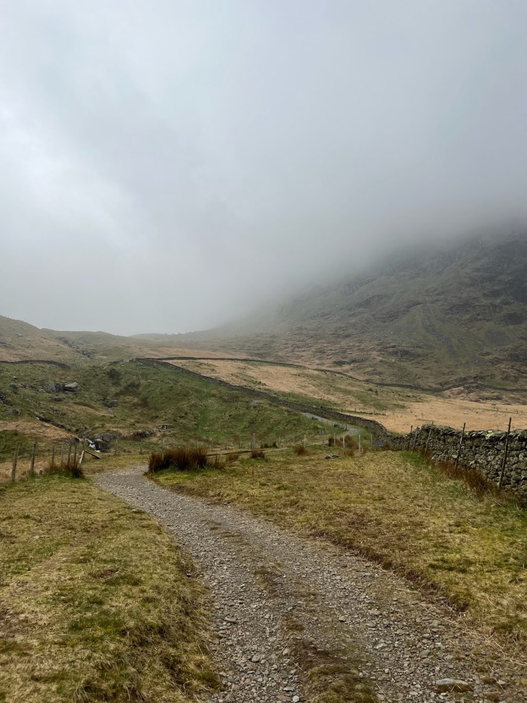 A stony path leading up the side of the fell. Thick cloud hides half of the fell top.