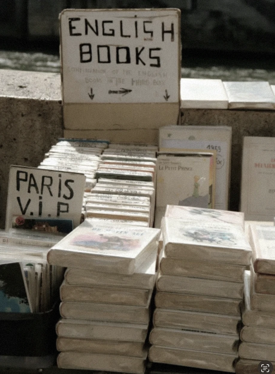Street bookstall by the Seine selling English novels, vintage covers stacked under soft Parisian light.