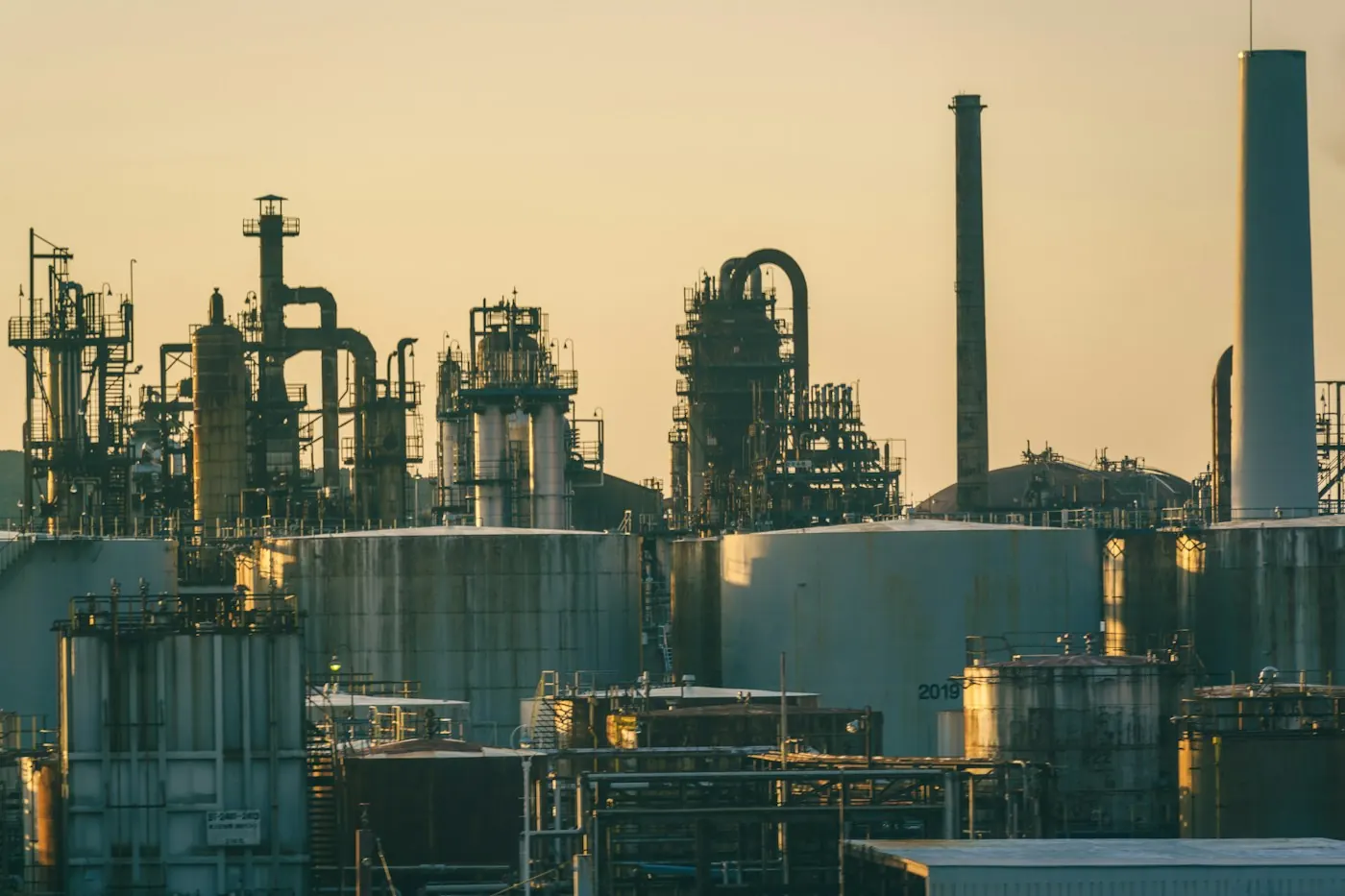 Oil refinery with storage tanks and chimneys under a golden sky