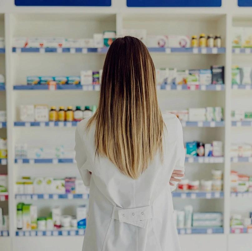 Pharmacist in a white coat reviewing products on shelves in a pharmacy
