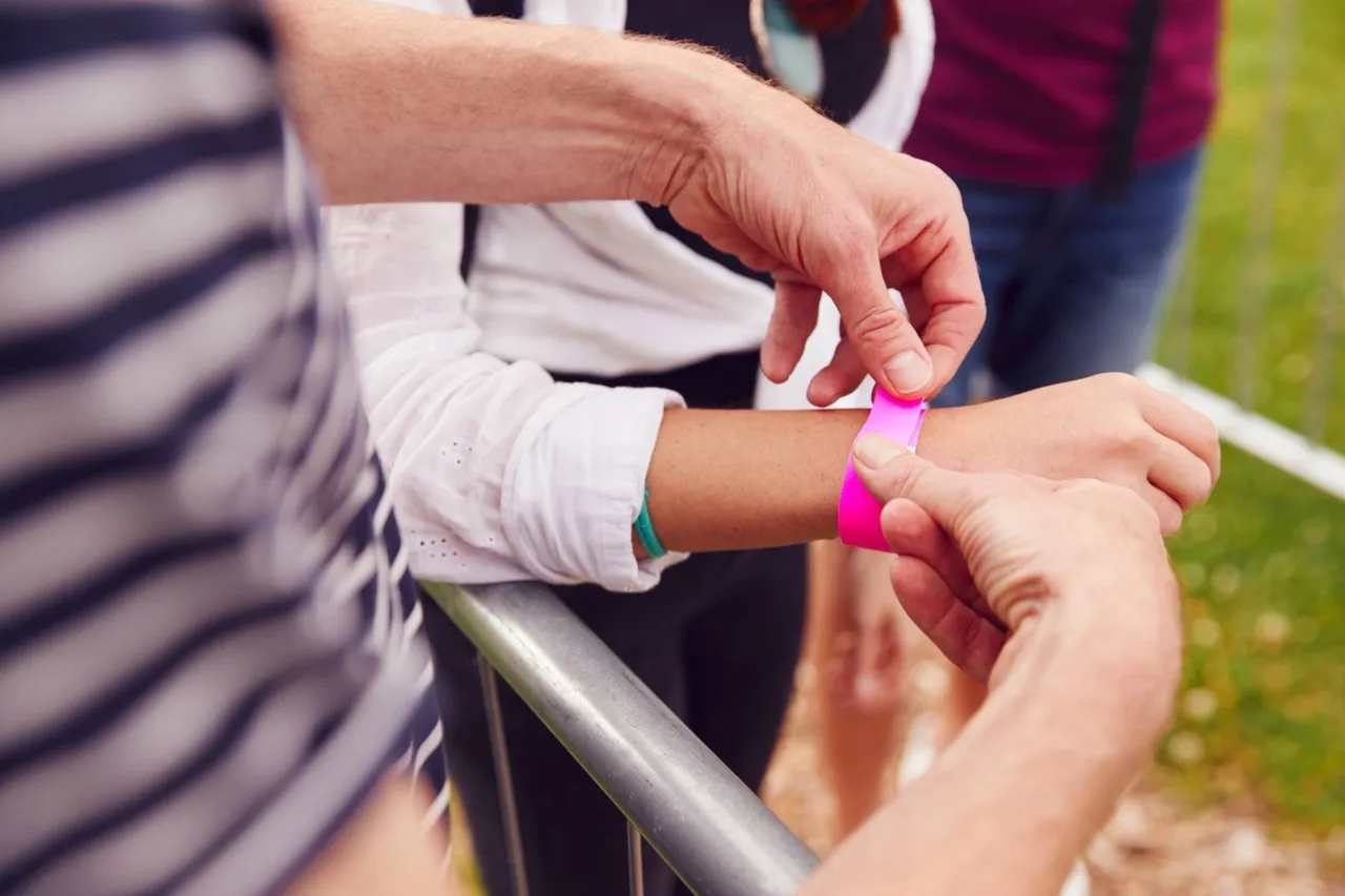 Closeup of someone putting a pink wristband on another person’s wrist.