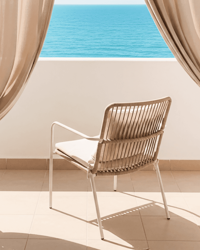 Minimalist balcony with a chair facing the ocean, framed by flowing curtains.
