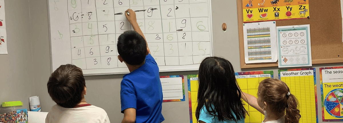 Children in an elementary math enrichment class solving math problems together on a classroom whiteboard.