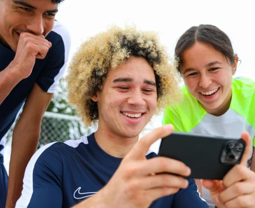 Youth soccer players smiling and enjoying game footage on a smartphone, showcasing Reeplayer’s mobile app for instant replay and analysis