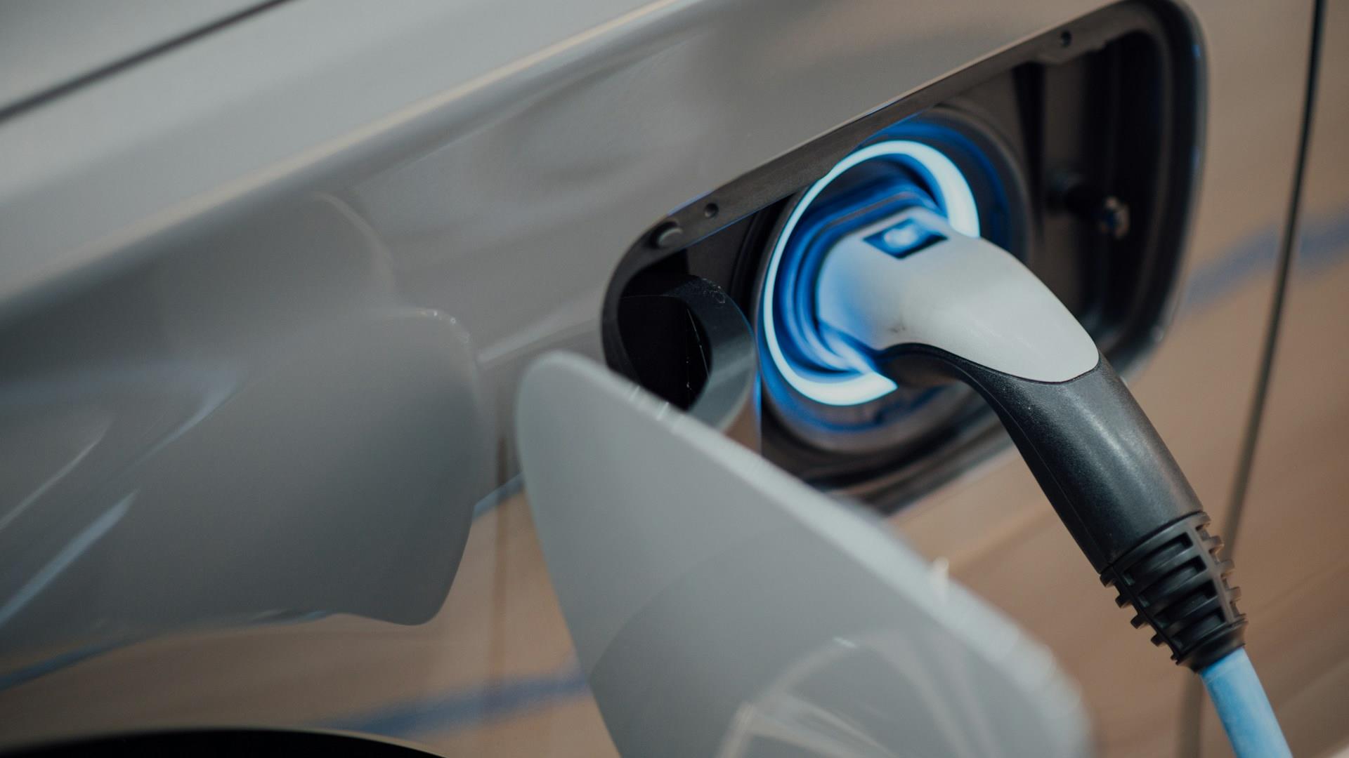 Close-up of an electric vehicle charging port with a plug inserted, emitting a soft blue light, illustrating clean energy and technology innovation.