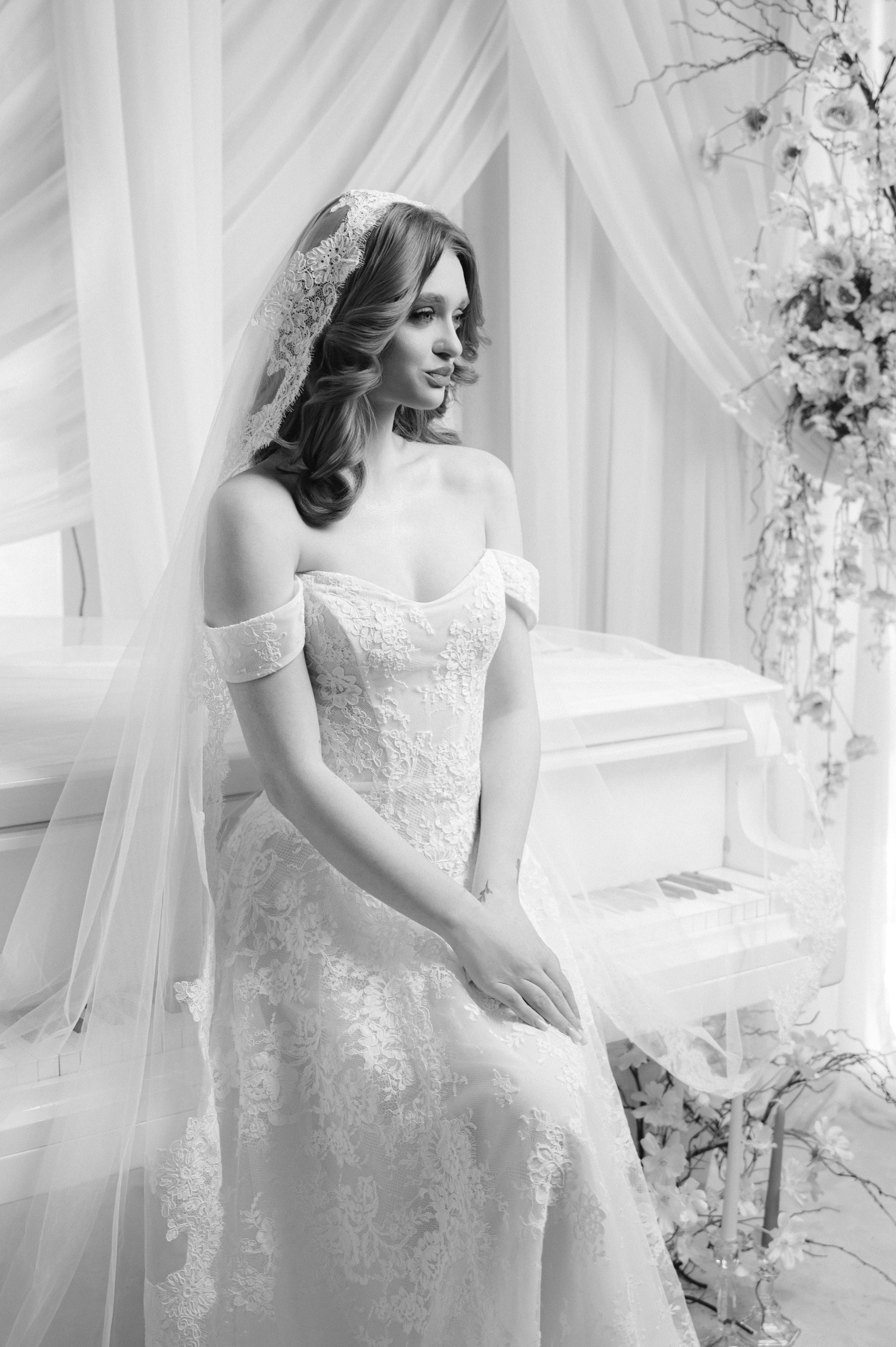 Portret alb-negru de mireasă așezată lângă pian într-un decor elegant, ședință foto bridal în București