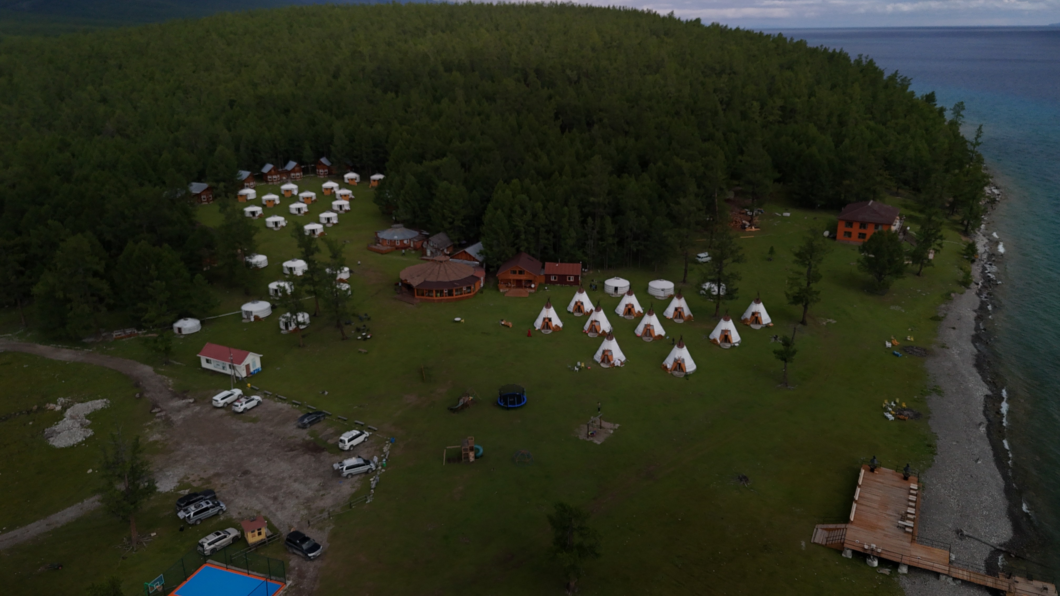 Smiling young woman with long hair standing against a dark green background, holding a finger to her chin.