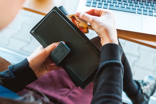 A person holds a black wallet and uses a smartphone while seated at a cozy cafe with wooden surfaces.