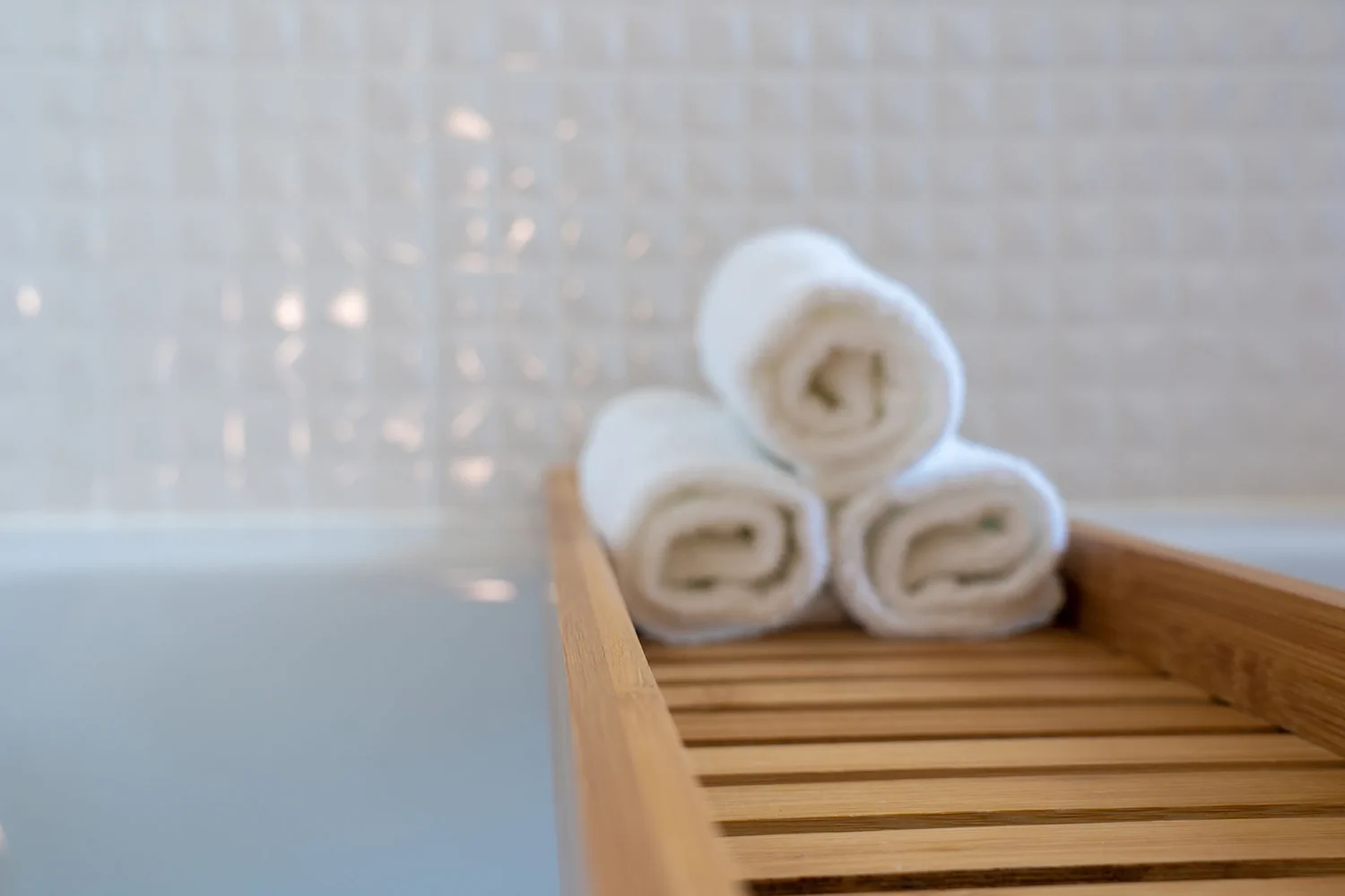 Rolled spa towels arranged on a wooden tray in a calm wellness setting.