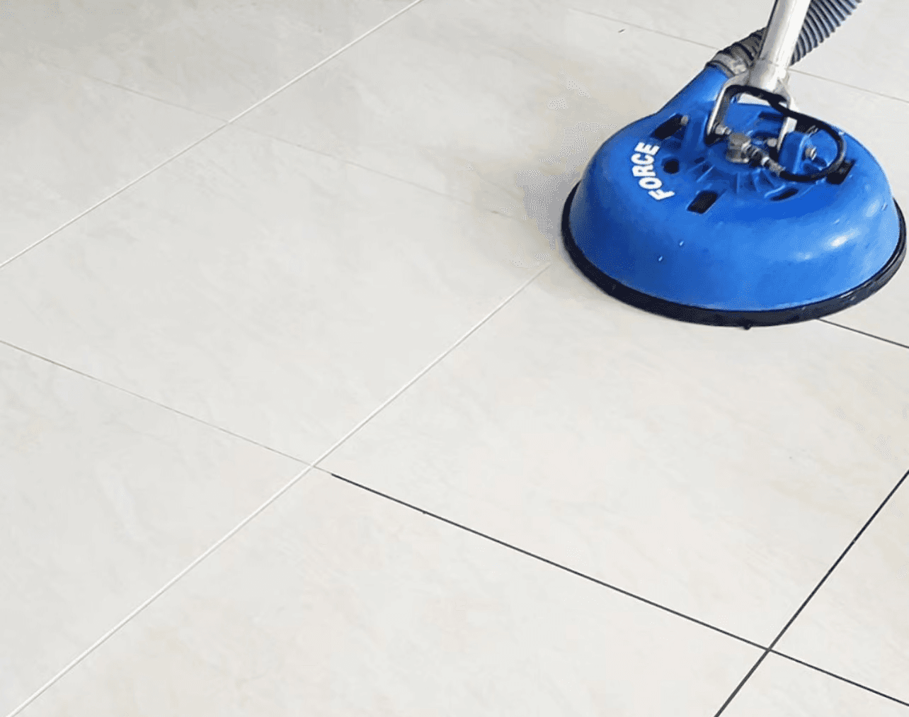 Vacuum cleaner on a carpet, tile floor being cleaned with a blue steam cleaning machine, and upholstery being cleaned with a vacuum attachment on a fabric surface.