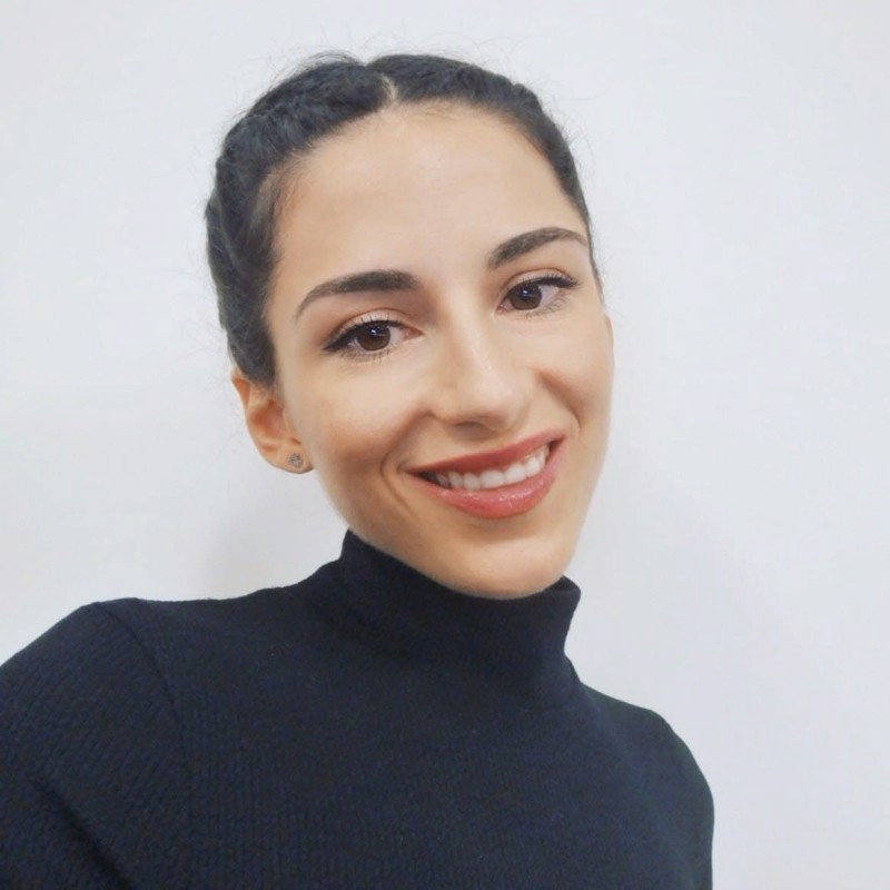 A person in a winter coat and furry hat walking along a snow-covered path through a forest of frosted trees.