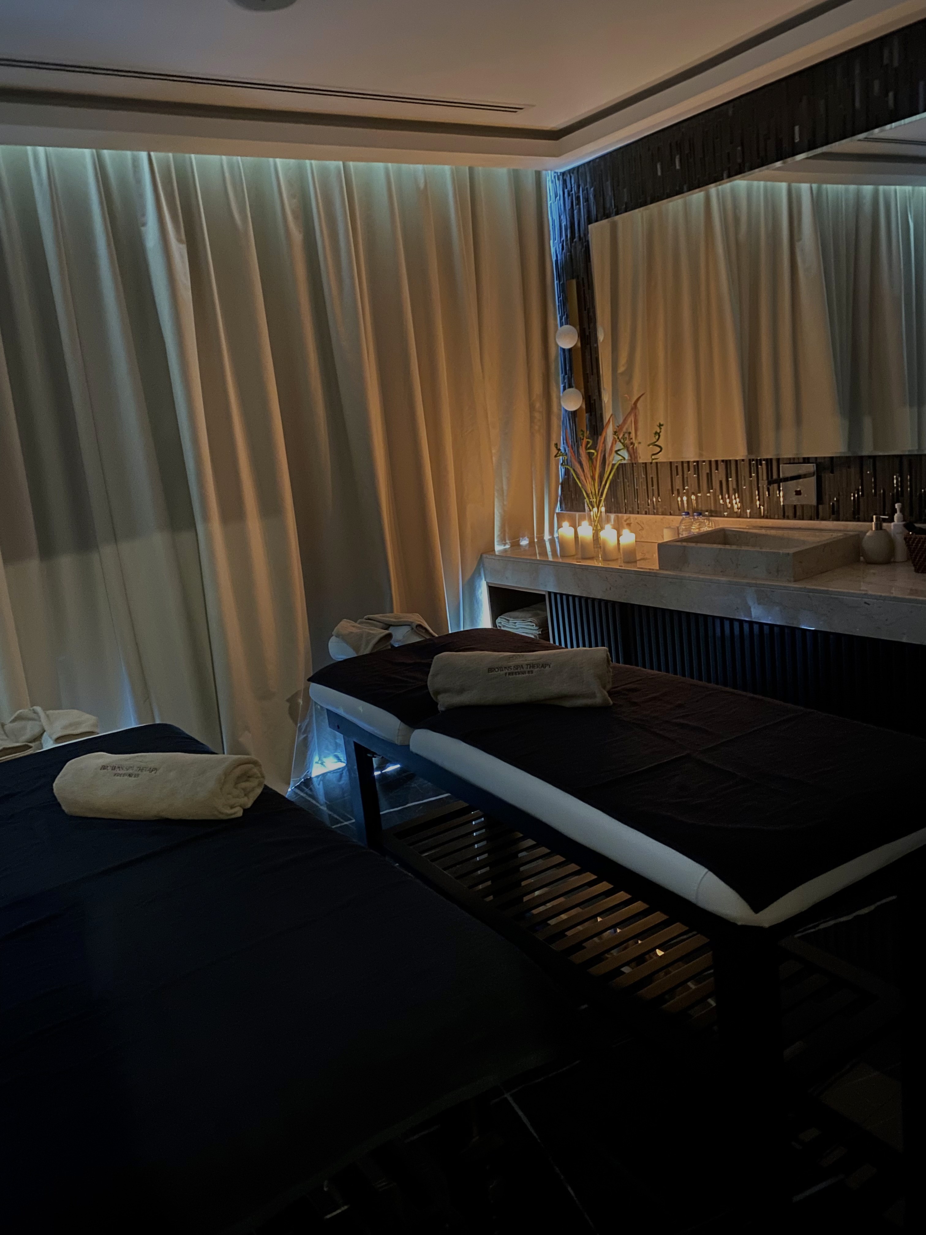 A luxurious indoor pool area with a panoramic view of a city at sunset. Comfortable lounge beds with soft fabrics surround the pool, while warm ambient lighting enhances the sophisticated atmosphere. The space combines modern elegance with a tranquil vibe.