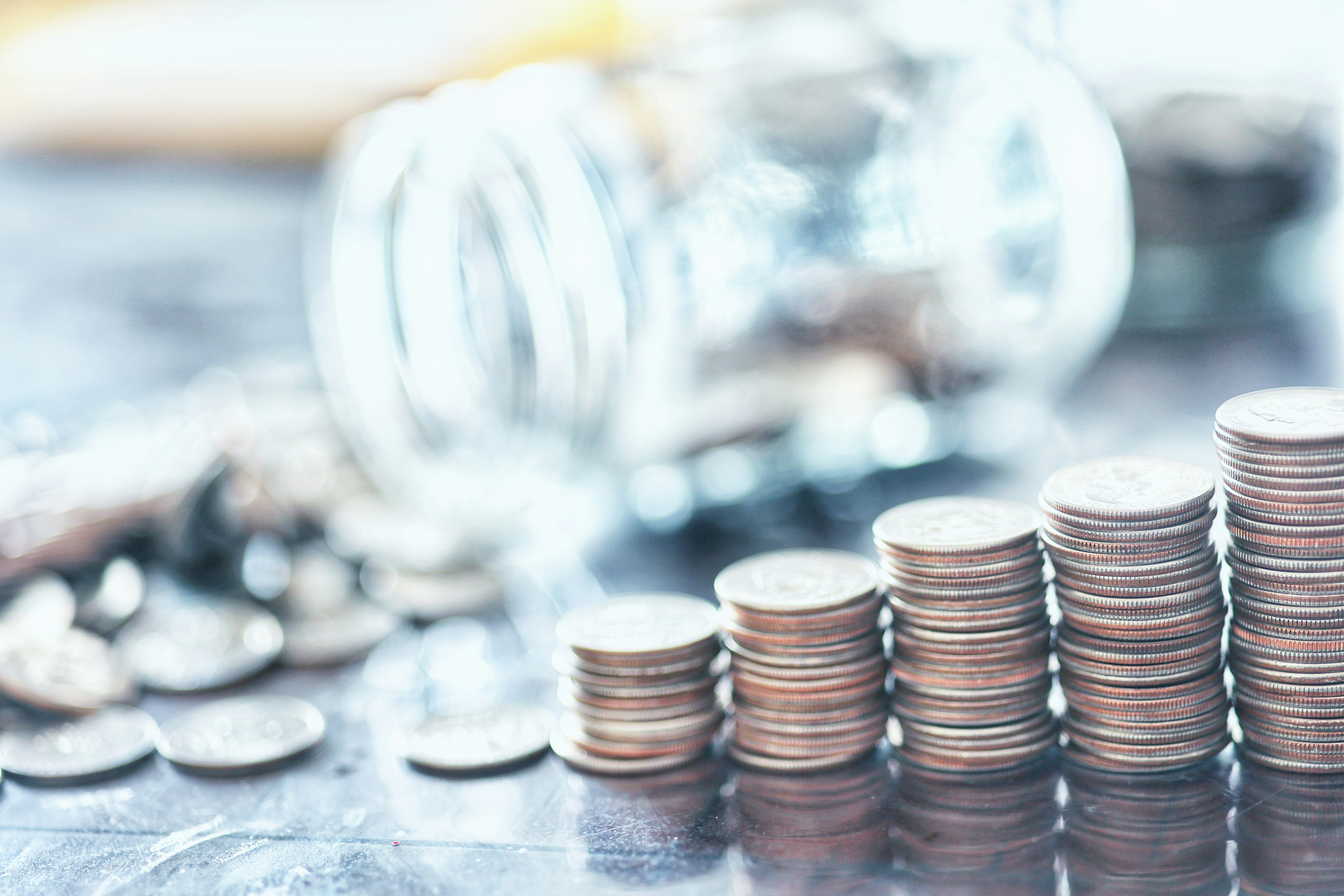 A stack of coins being budgeted. A glass jar is in the background tipped over with coins falling out.