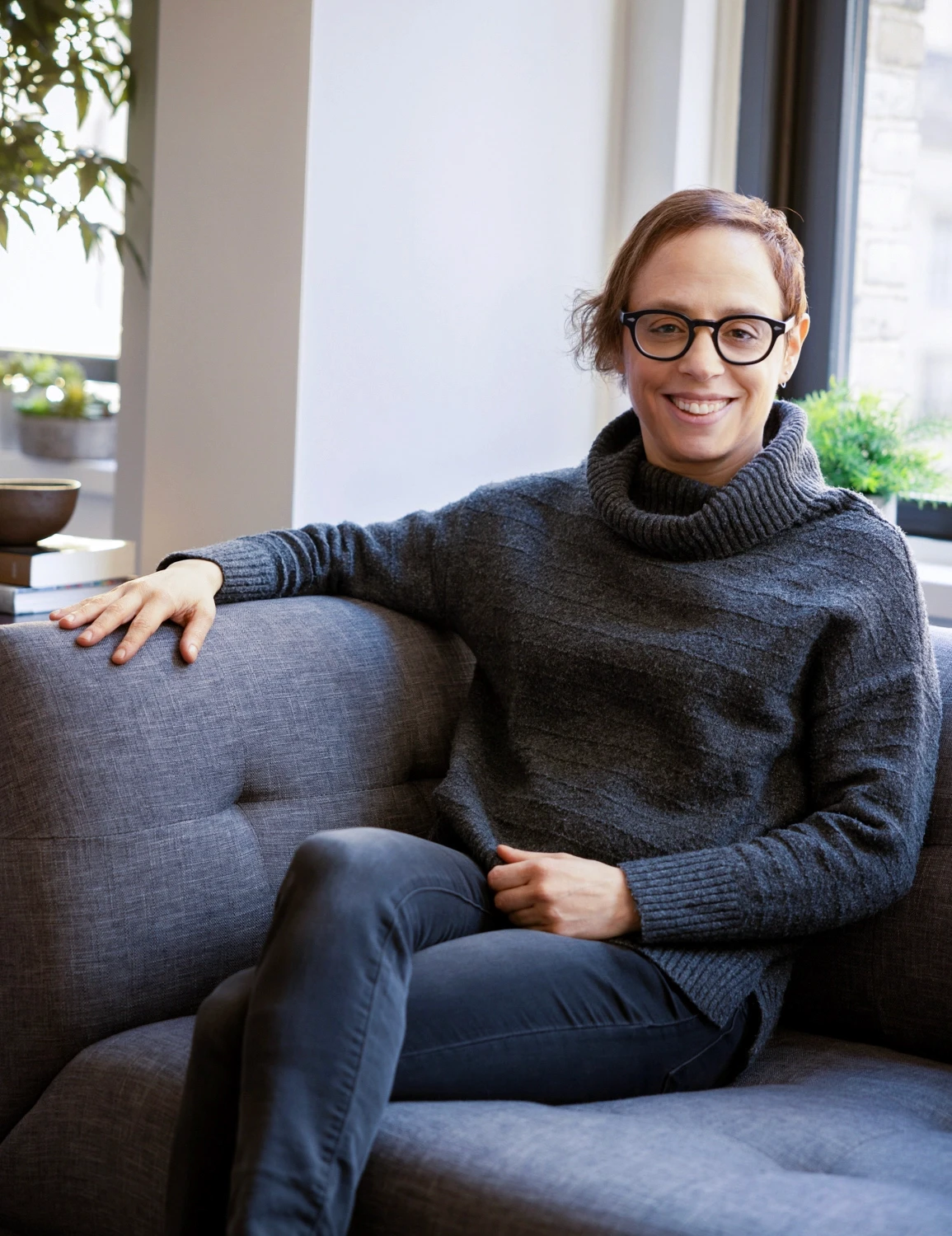 a relaxed and approachable therapist sitting in a warmly lit room with a cozy couch and a potted plant with a window overlooking los angeles symbolizing excellent client reviews and high satisfaction for polyamory therapy in Los Angeles.