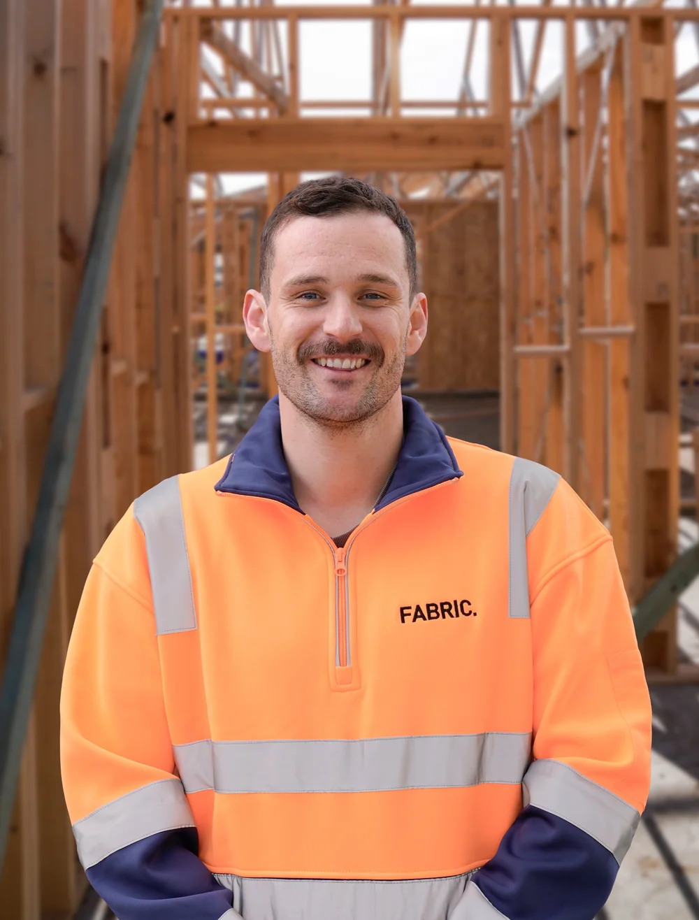 Construction worker in high-visibility jacket smiling on a building site.