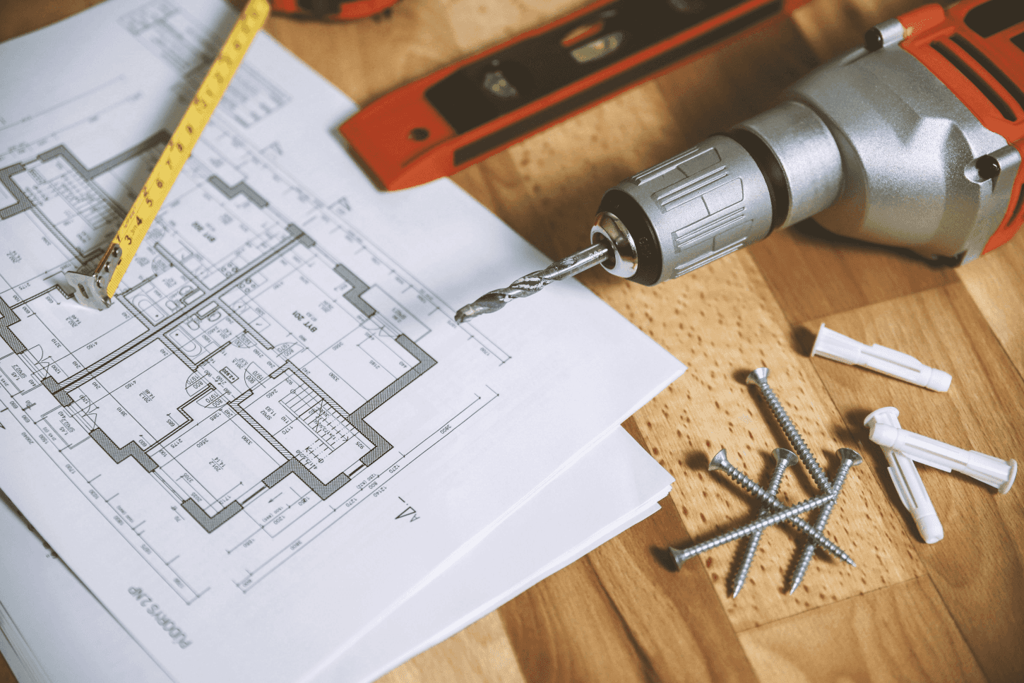 Home renovation tools on architectural blueprint with drill, screws, and measuring tape.