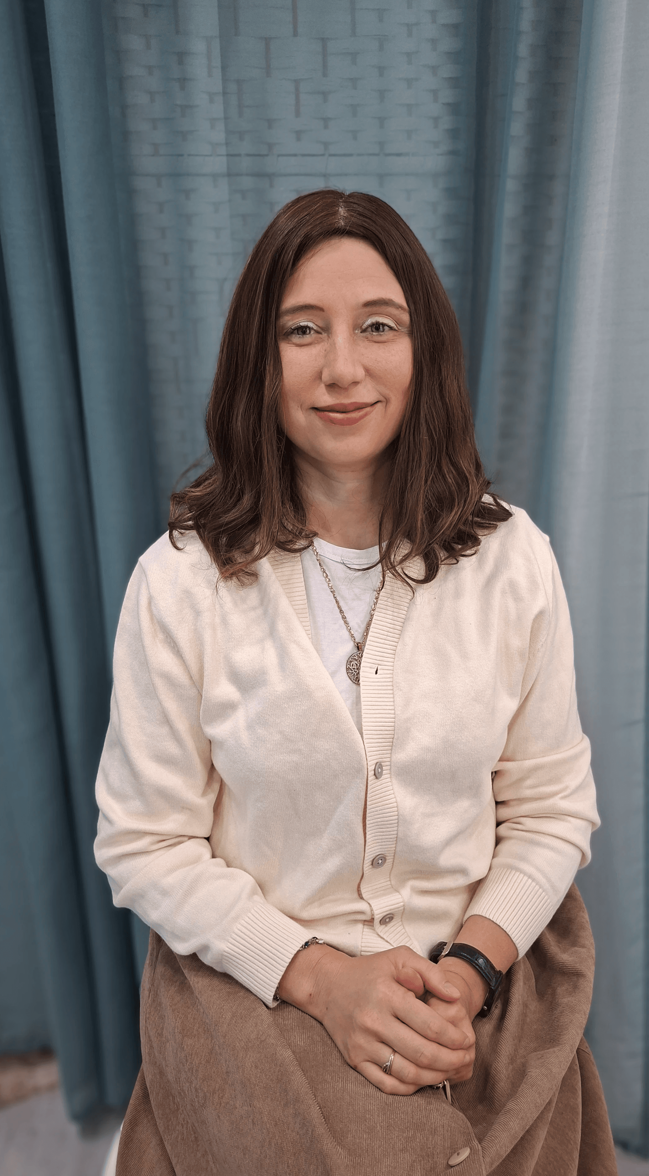 Smiling female therapist with short gray hair, wearing a brown top and a purple shawl, surrounded by a cozy background.