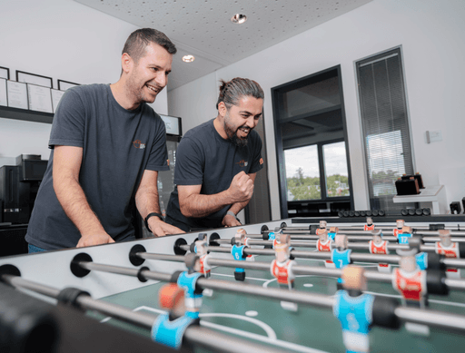 Two men laughing while playing foosball. One man is celebrating with a fist pumped in the air.