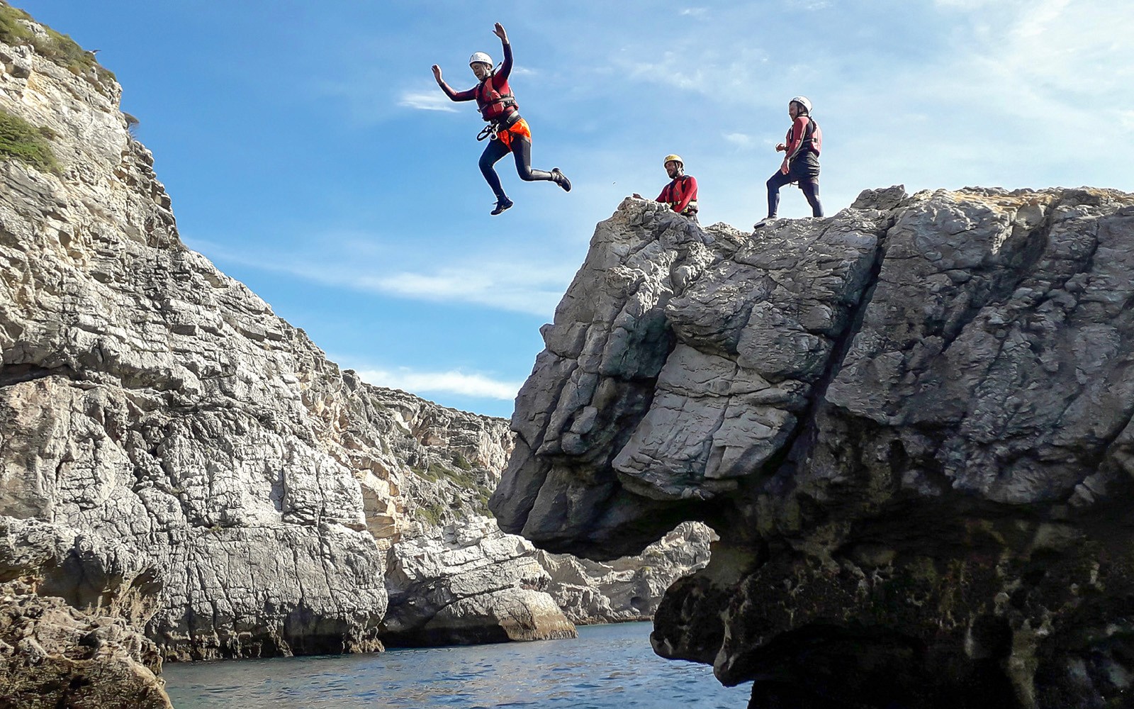 Deltakere i klippeklatring hopper fra steinete stup ned i sjøen.