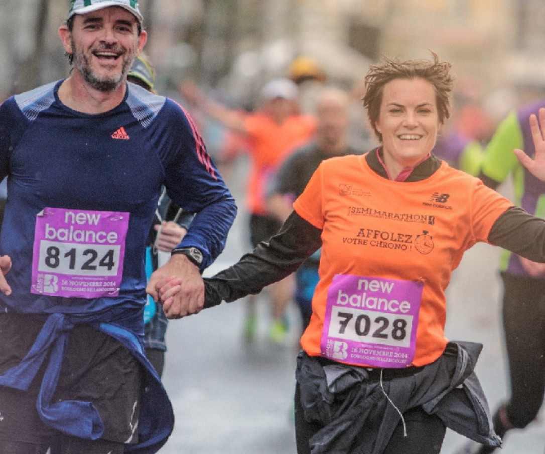 Un homme et une femme en tenue de course participent à une course. Ils sourient et se tiennent la main, traversant un moment agréable tout en courant.