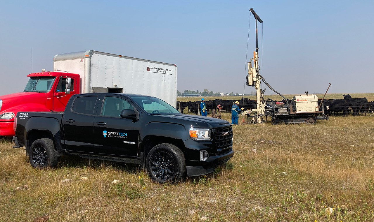 SweetTech branded truck at Rocky Ridge Farms geotechnical drilling site in Irricana with drill rig and crew conducting field investigation in prairie grassland
