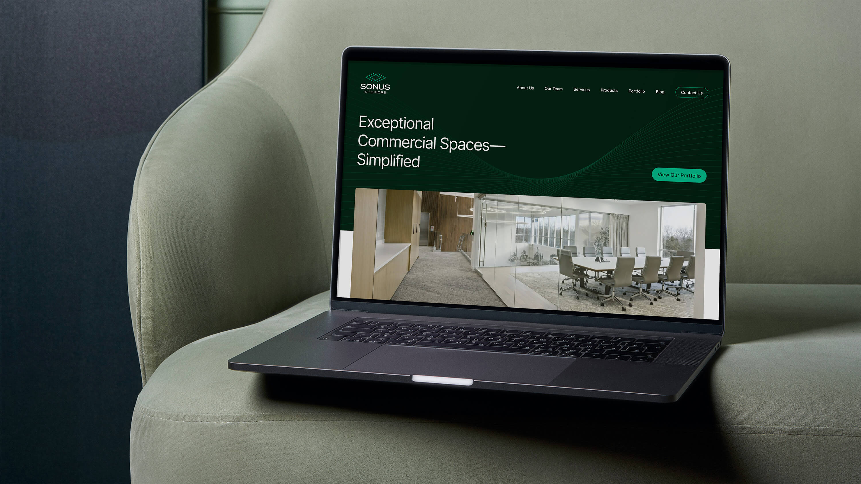 Macbook Pro laptop showing the Sonus Interiors homepage resting on a minimal light green cushioned chair. 