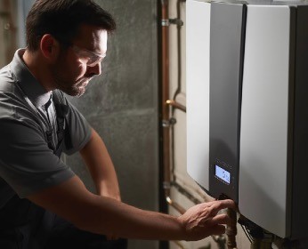 A man in a gray shirt interacts with a control panel in a dimly lit space.