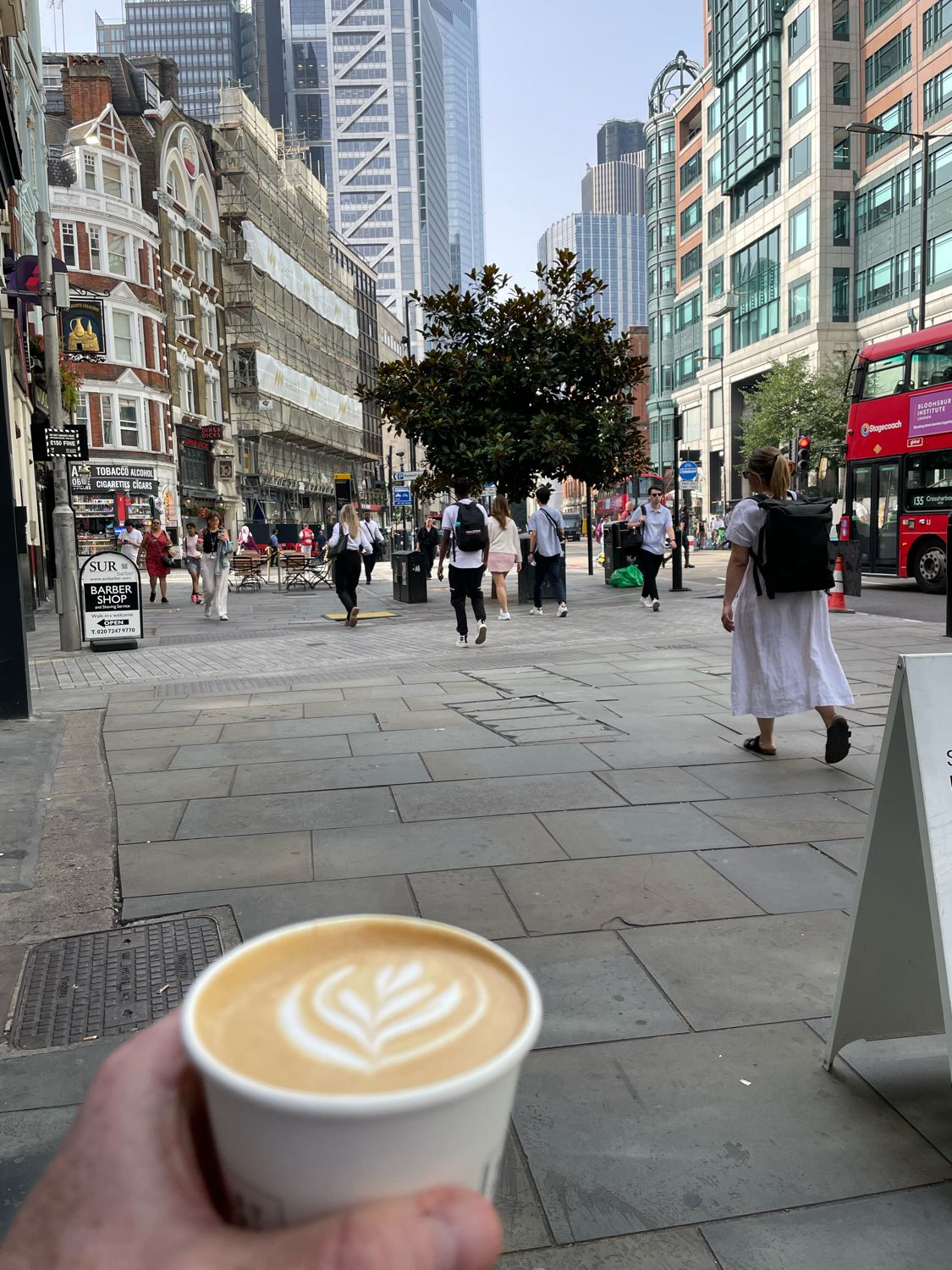 Coffee cup with latte art held in front of a bustling urban street scene at the Cue London office.