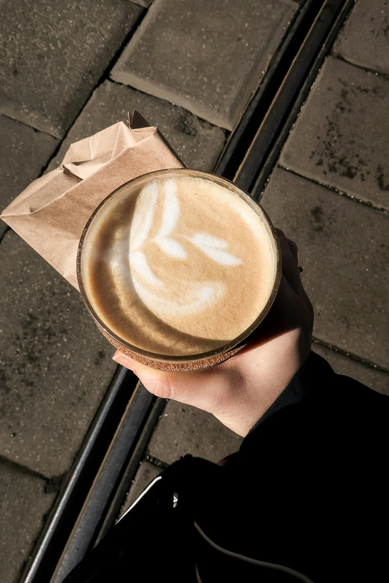 A hand holding a takeaway coffee with latte art.