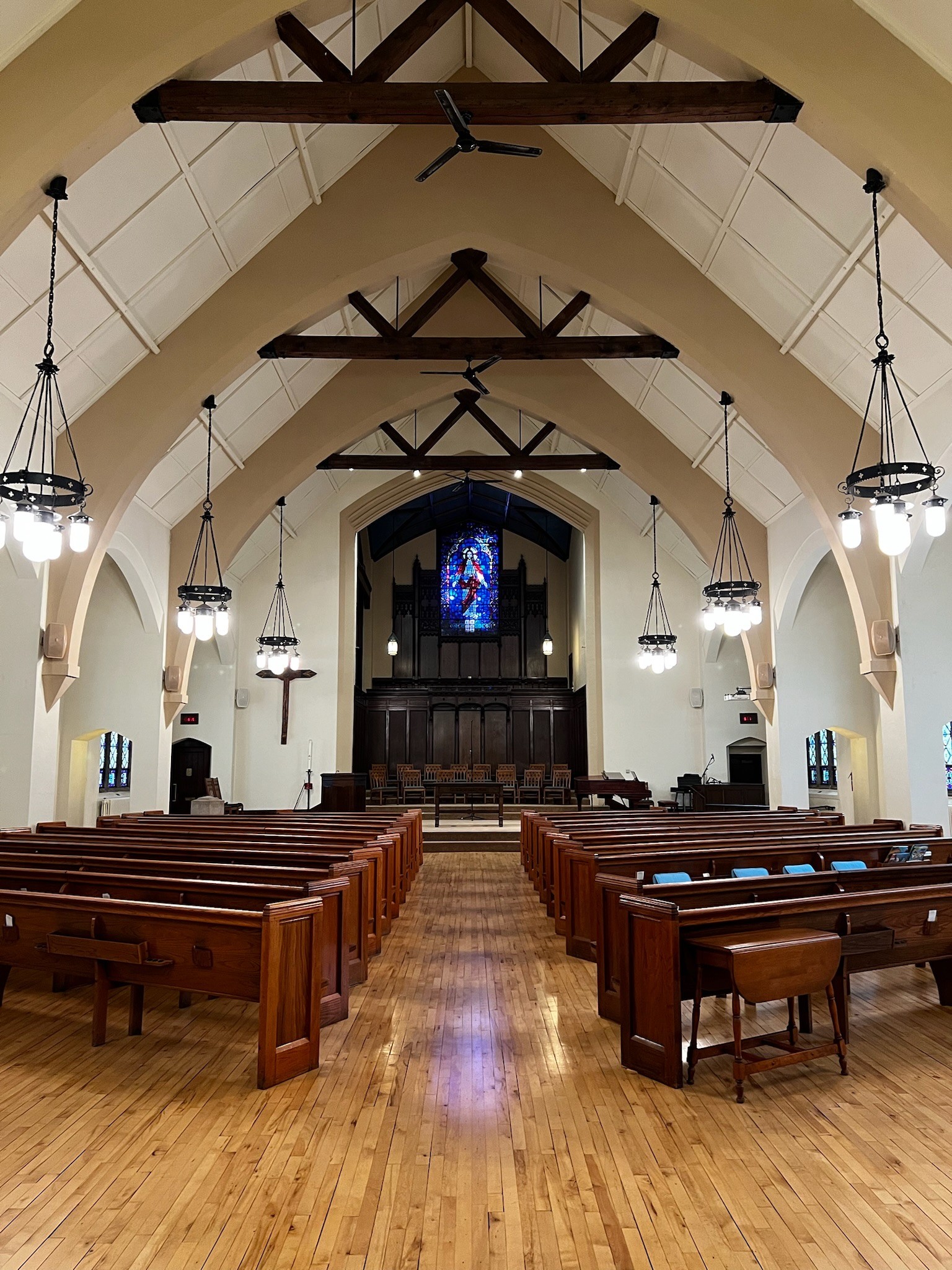 Grace Trinity Church sanctuary with wooden pews, high vaulted ceilings, hanging chandeliers, and a large stained glass window depicting Jesus.