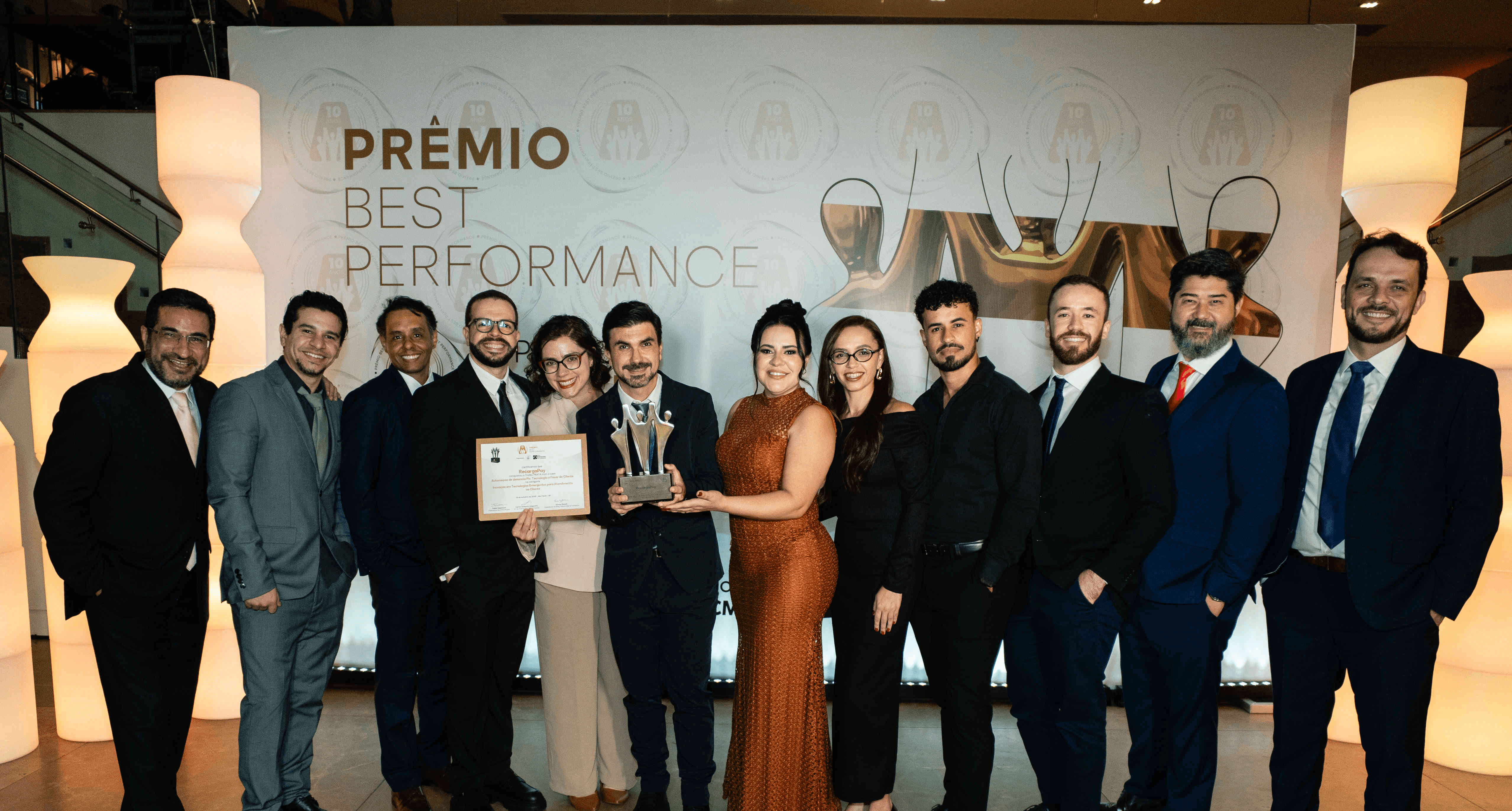 Executivos da RecargaPay posando com troféu prata e certificado no palco do Prêmio Best Performance 2025